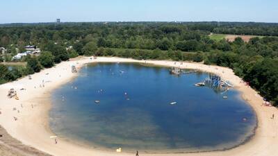 The large recreational lake with a sandy beach and play equipment at the Witterzomer holiday park