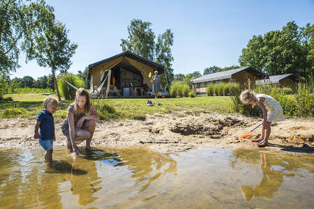 Children play in the water of the lake at the safari tents at Camping Vreehorst