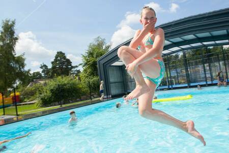 Girl jumps into the outdoor pool of holiday park Camping de Norgerberg