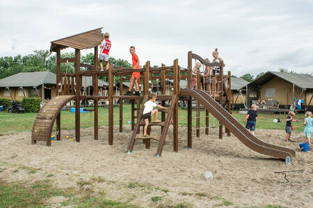 Children play in a playground on a field with safari tents at holiday park De Boshoek