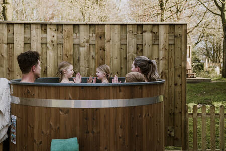 A family is sitting in the hot tub in the garden of a bungalow at the Dierenbos holiday park