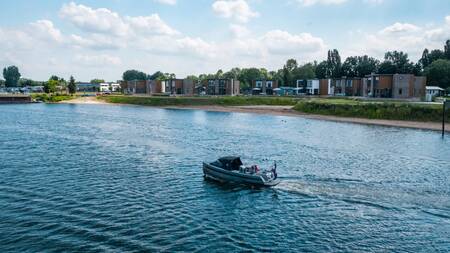 A sloop sails in front of holiday homes on the water at the EuroParcs Aan de Maas holiday park