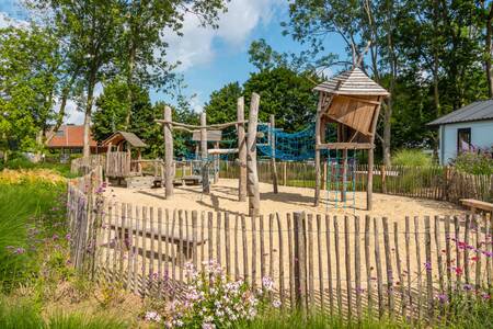A fenced playground with wooden play equipment at holiday park EuroParcs Aan de Maas