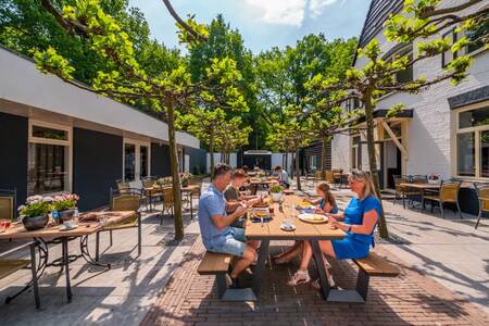 The family eats on the terrace of the restaurant at the EuroParcs De Hooge Veluwe holiday park