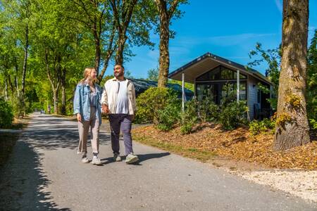 A couple walks in front of a holiday home at the EuroParcs De Wije Werelt holiday park