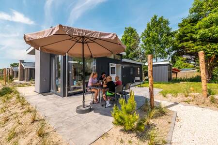 The family is sitting at a table in the garden of a holiday home at the EuroParcs Poort van Zeeland