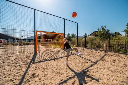 Boy playing football on the sports field at the EuroParcs Poort van Zeeland holiday park