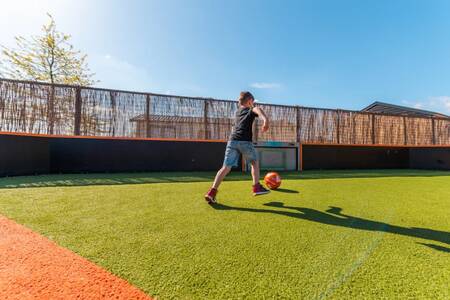 Child playing football on the playing field of holiday park EuroParcs Veluwemeer