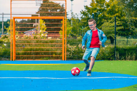 Boy playing football on the playing field at holiday park EuroParcs Zuiderzee