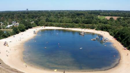 The large recreational lake with a sandy beach and play equipment at the Witterzomer holiday park