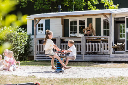 Children play in front of a chalet with a covered veranda at the Kampeerdorp de Zandstuve park