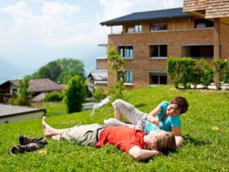 2 people lie on the grass in front of an apartment complex at Landal Alpen Chalet Matin