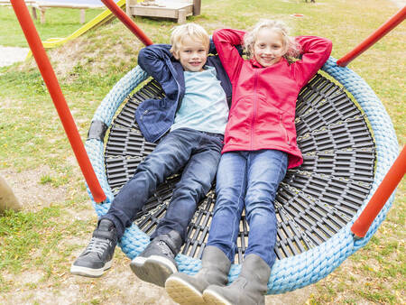 2 children on a swing in a playground at the Landal Hochwald holiday park