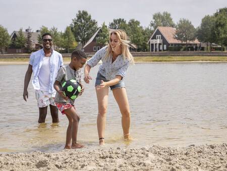 Family plays in the water of the recreational lake at the Landal Hof van Saksen holiday park