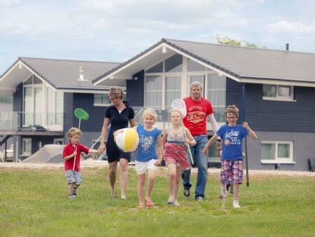 Family walks on a lawn in front of holiday homes at Landal Waterpark Sneekermeer