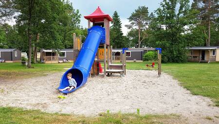 Child on the slide in a playground between chalets at holiday park Molecaten Park De Koerberg