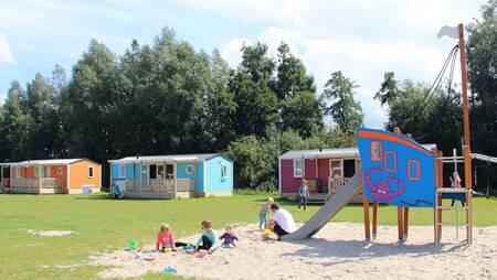 Chalets of the "Pioen" type on a field with a playground at holiday park Molecaten Park Flevostrand