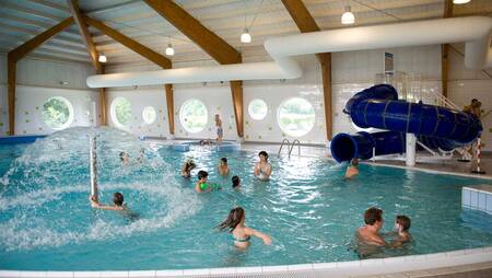 People swimming in the indoor pool with slide at holiday park Molecaten Park Flevostrand