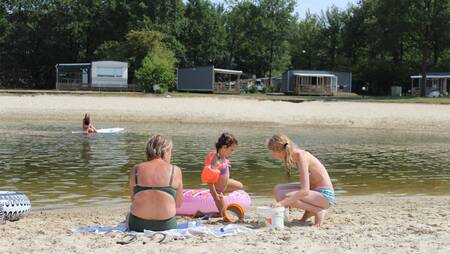 Family playing in the sand of the recreational lake at Molecaten Park Kuierpad holiday park