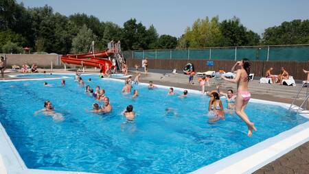 People swim in the outdoor pool with a red slide at the Molecaten Park Rondeweibos holiday park