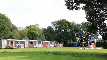 Chalets of the "Pioen" type on a field with a playground at holiday park Molecaten Park 't Hout