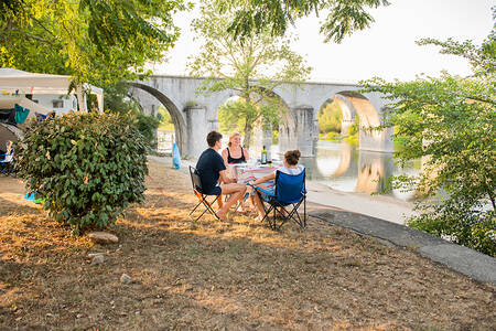 People sit next to the river Ardèche at holiday park RCN La Bastide en Ardèche