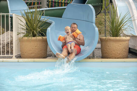 Man and child slide down the slide in the swimming pool of holiday park RCN La Bastide en Ardèche