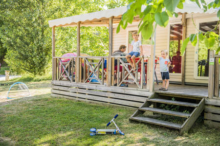 Family is sitting on the covered veranda of a mobile home at RCN Le Moulin de la Pique holiday park