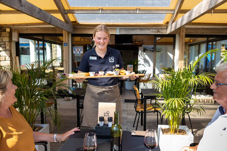 Waiter delivers snacks to a couple on the terrace of the restaurant at holiday park RCN Port l'Epine