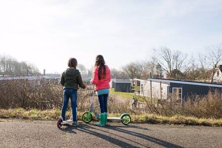 2 children on scooters in front of chalets at holiday park RCN Toppershoedje