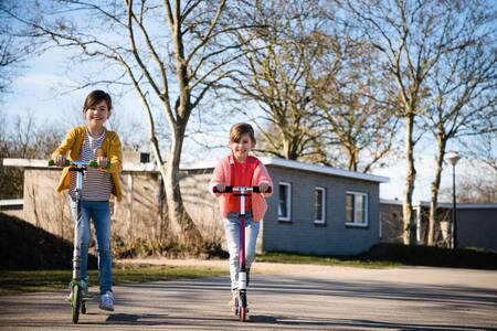 Two children scooter in front of chalets at the RCN Toppershoedje holiday park