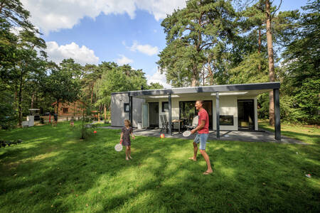 Father and daughter play tennis in the garden of a holiday home at holiday park RCN het Grote Bos