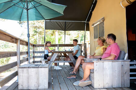 The family sits on the veranda of a safari tent at the RCN les Collines de Castellane holiday park