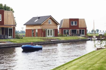 A sloop sails in front of holiday homes on the water at holiday park Recreatiepark Tusken de Marren