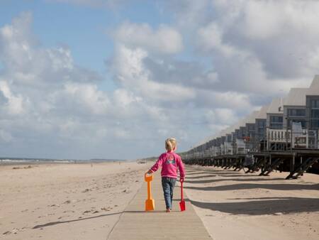 Child walks on the beach in front of beach houses at Roompot Strandhuisjes Julianadorp