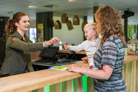 Woman with child receives key at the reception of Roompot Bungalowpark Hoenderloo