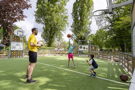 Father with 2 children playing on the multifunctional sports field of Roompot Château des Marais