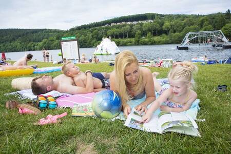 People lie on the grass at the reservoir next to Roompot Eifelpark Kronenburger See