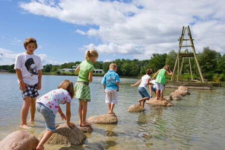 Children play on stones in the recreational lake of Roompot Holiday Park Hunzedal