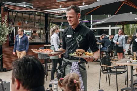 A waiter brings dinner to the terrace of Roompot Vakantiepark Kijkduin