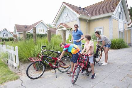 Family with bicycles in front of a holiday home at the Roompot Noordzee Résidence De Banjaard