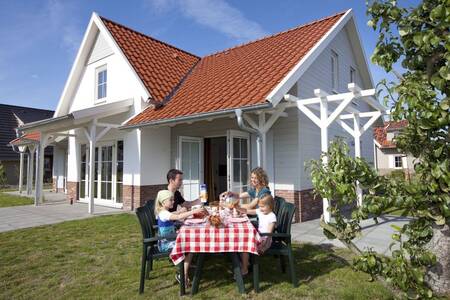 Family eats at a table in the garden of a holiday home at Roompot Résidence Klein Vink