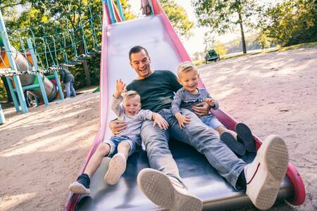 Father with 2 children on a slide in a playground at Roompot Vakantiepark Weerterbergen