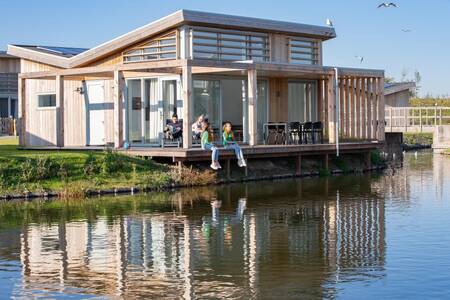 People on the terrace directly on the water of a holiday home at the Roompot Water Village